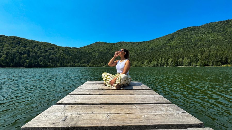 Discover Harghita - Woman sitting on wooden decking by Lake Sfânta Ana, volcanic lake surrounded by pine forests in Harghita County, Romania.