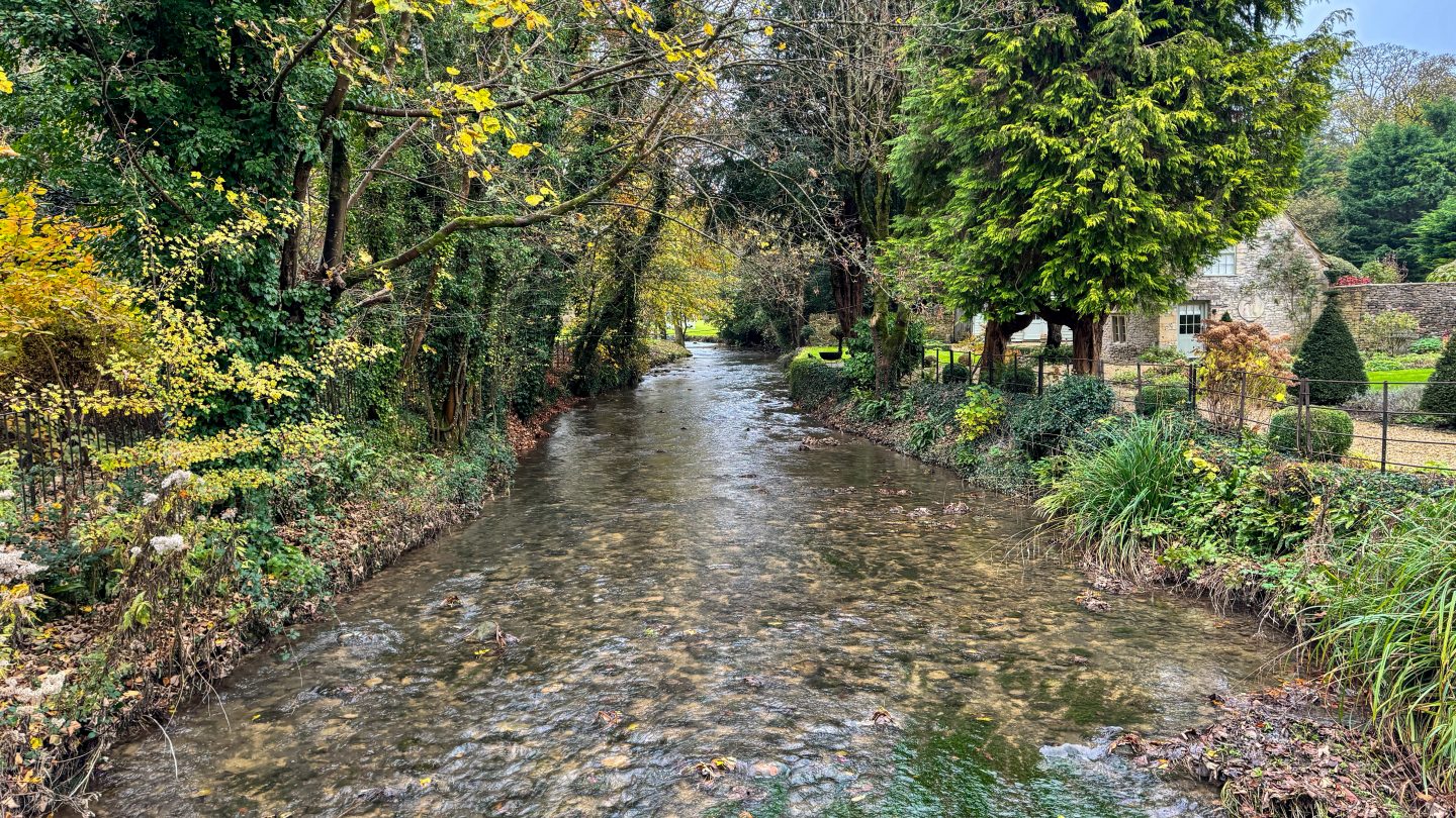 The peaceful Bybrook River flowing under a medieval stone bridge in the heart of Castle Combe village.