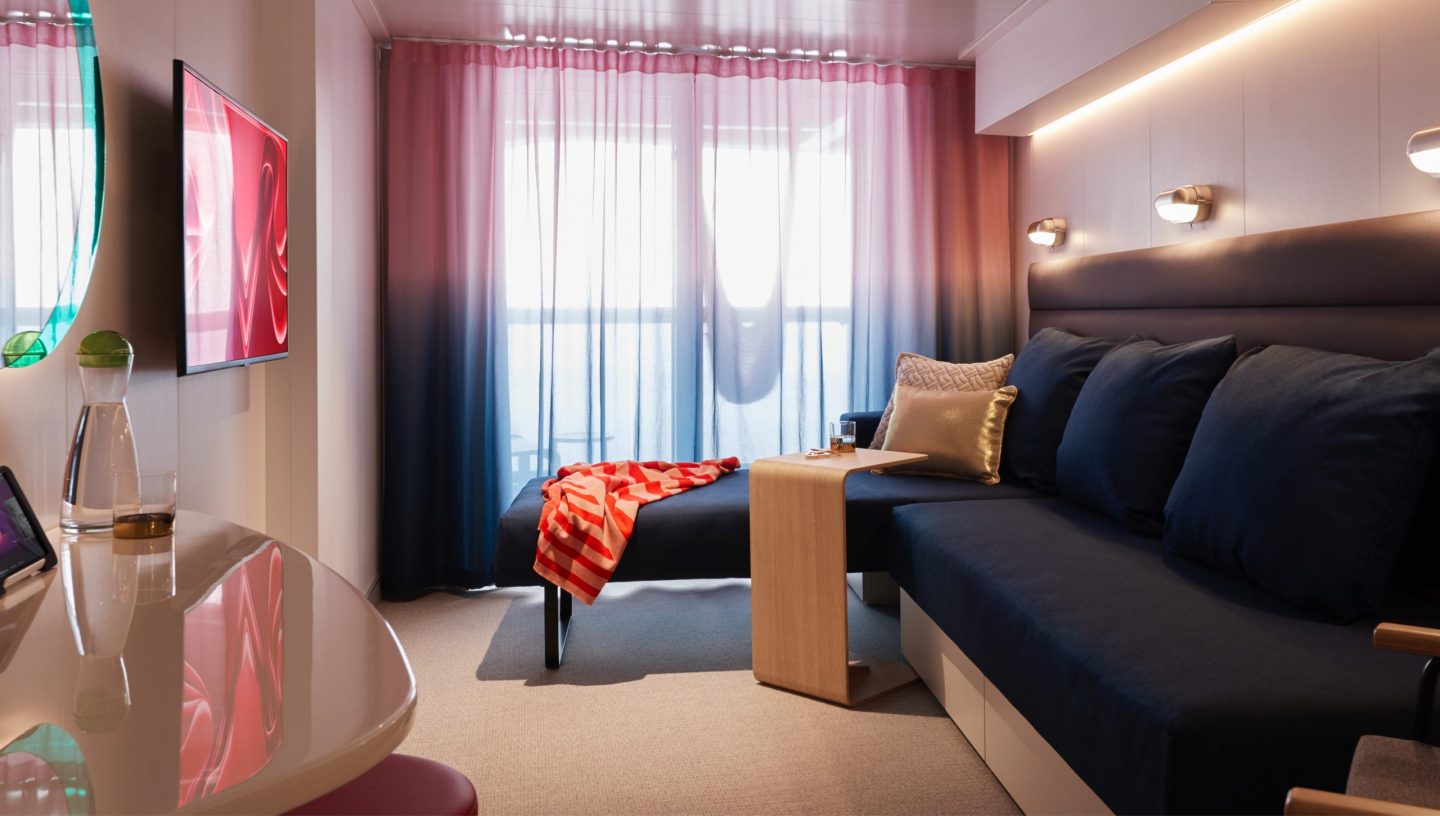 Interior of a Virgin Voyages cruise cabin showing bed, storage space and modern design