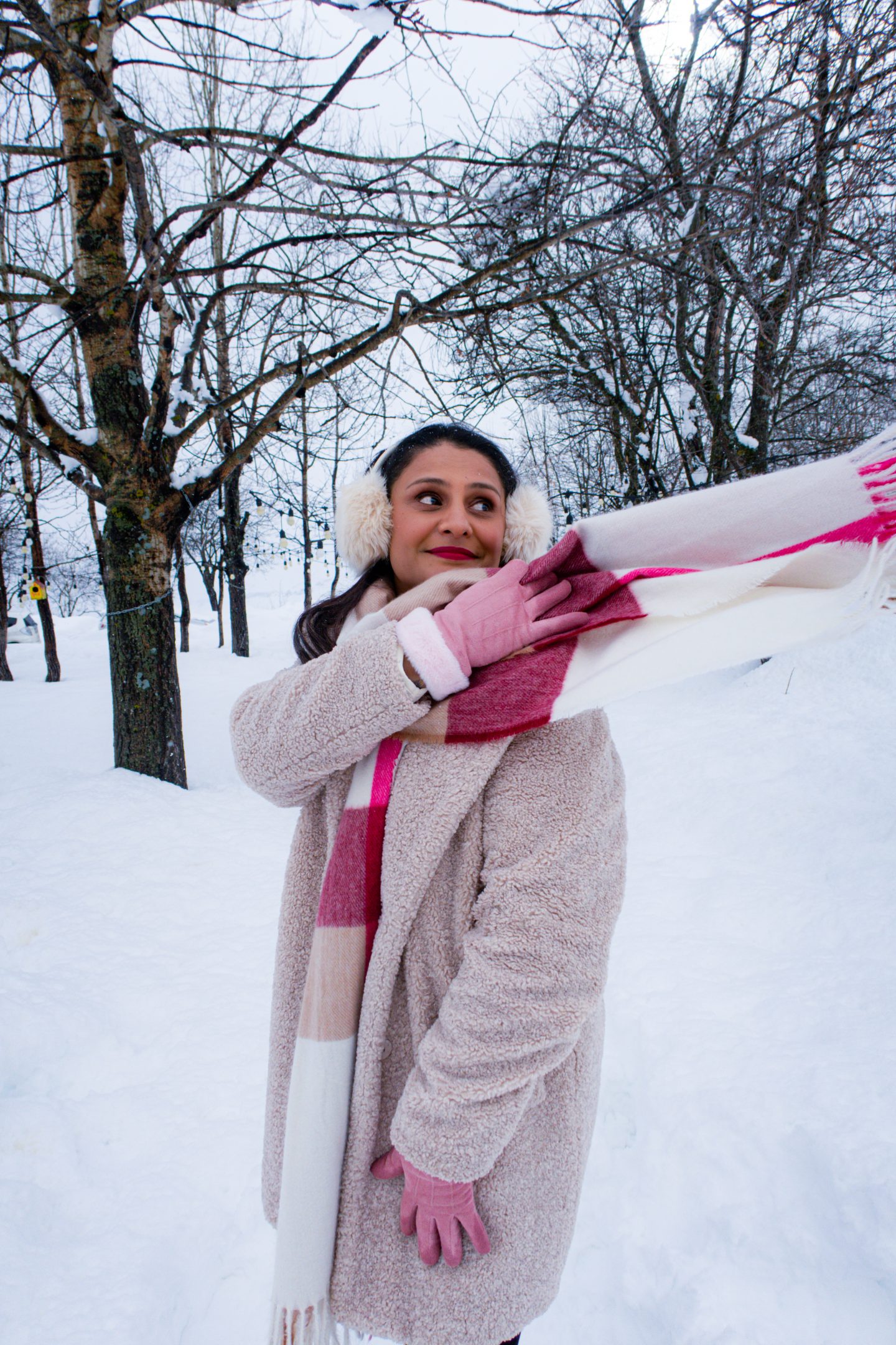 Woman wearing ear muffs, gloves and a woolly coat standing in the snow in Gudauri and throwing her scarf over her shoulder