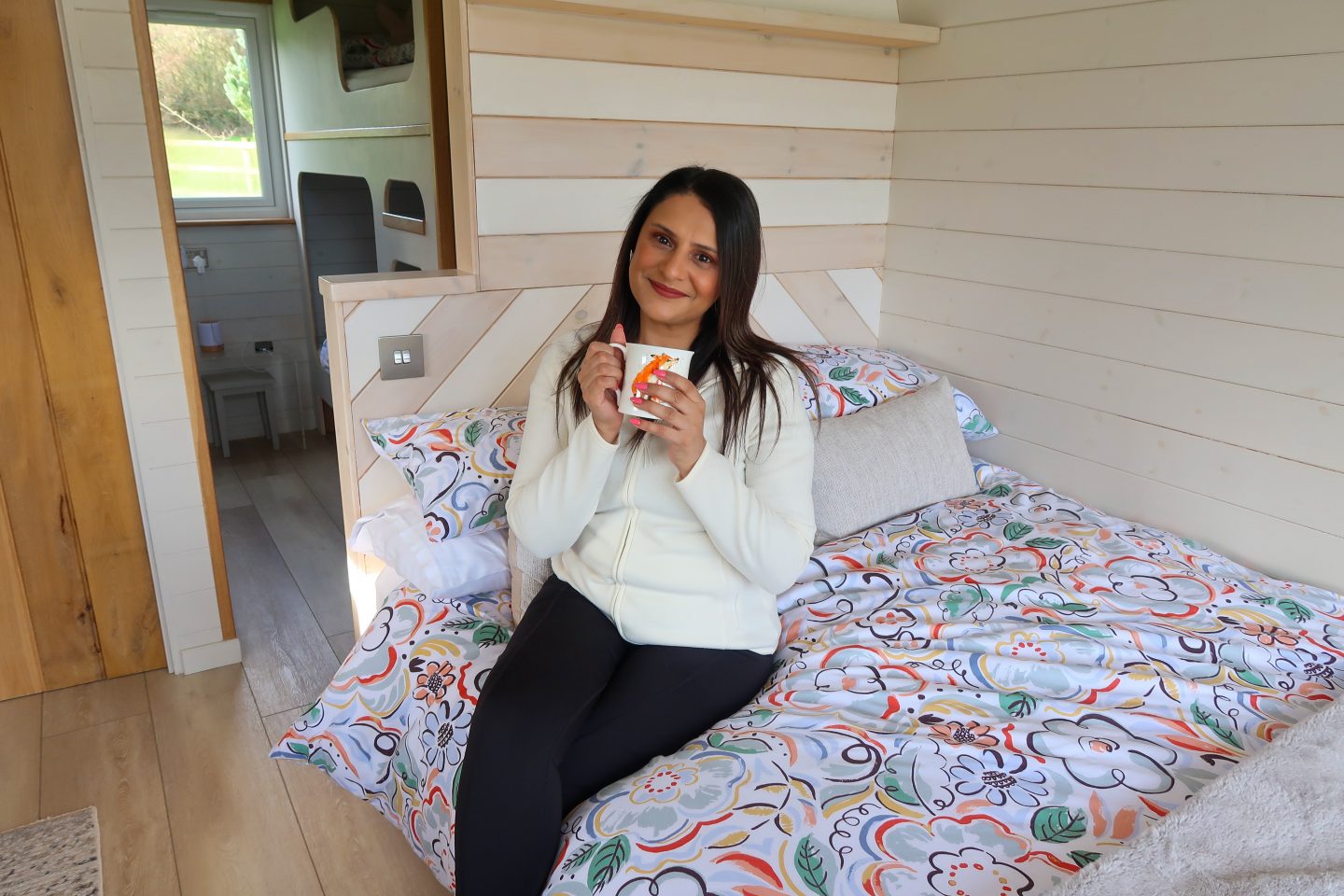 A woman sips a cup of tea in a luxury glamping pod at 3Trees in Matlock