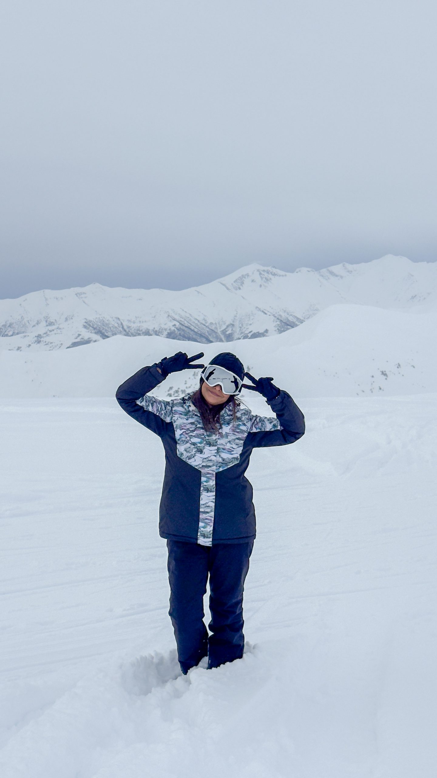 Woman standing in the snow in ski gear making a peace sign