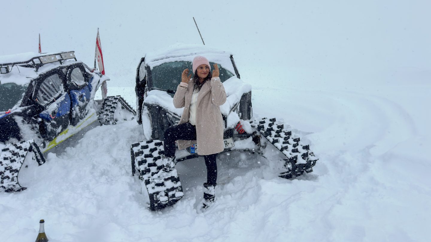 Woman standing with a snow buggy in the snow wearing a hat, gloves and woolly coat