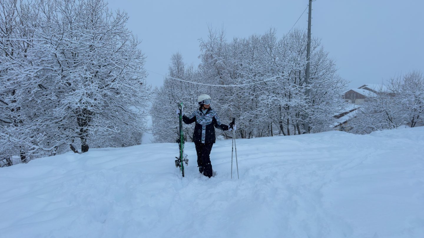 A woman standing with skis and poles, helmet and goggles ready for her first time skiing in Gudauri