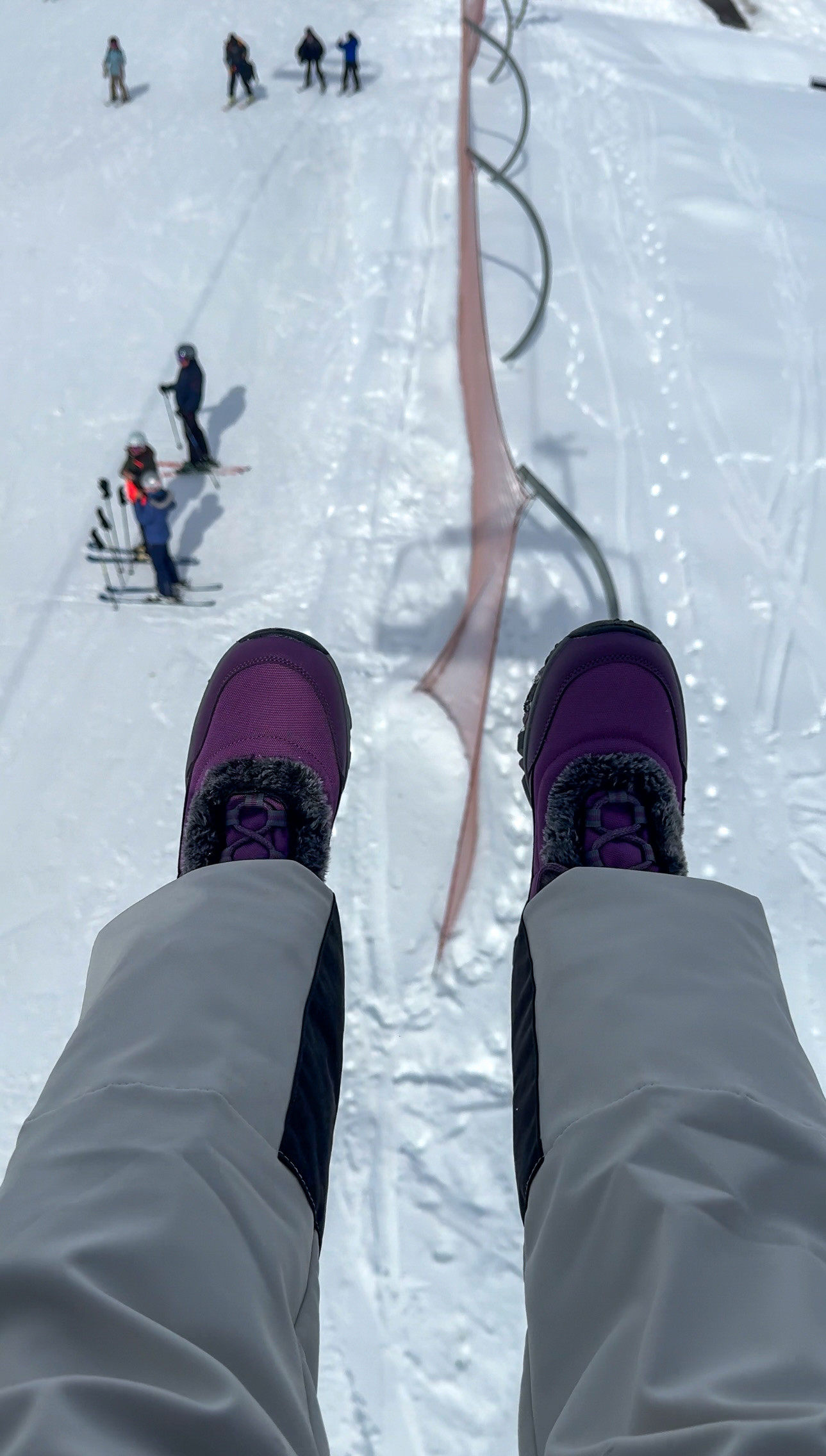 Girl's boots on a chair lift with skiers beneath