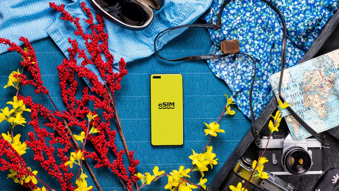 Flatlay of travel essentials like a map, sunglasses and camera with a phone showing an eSim
