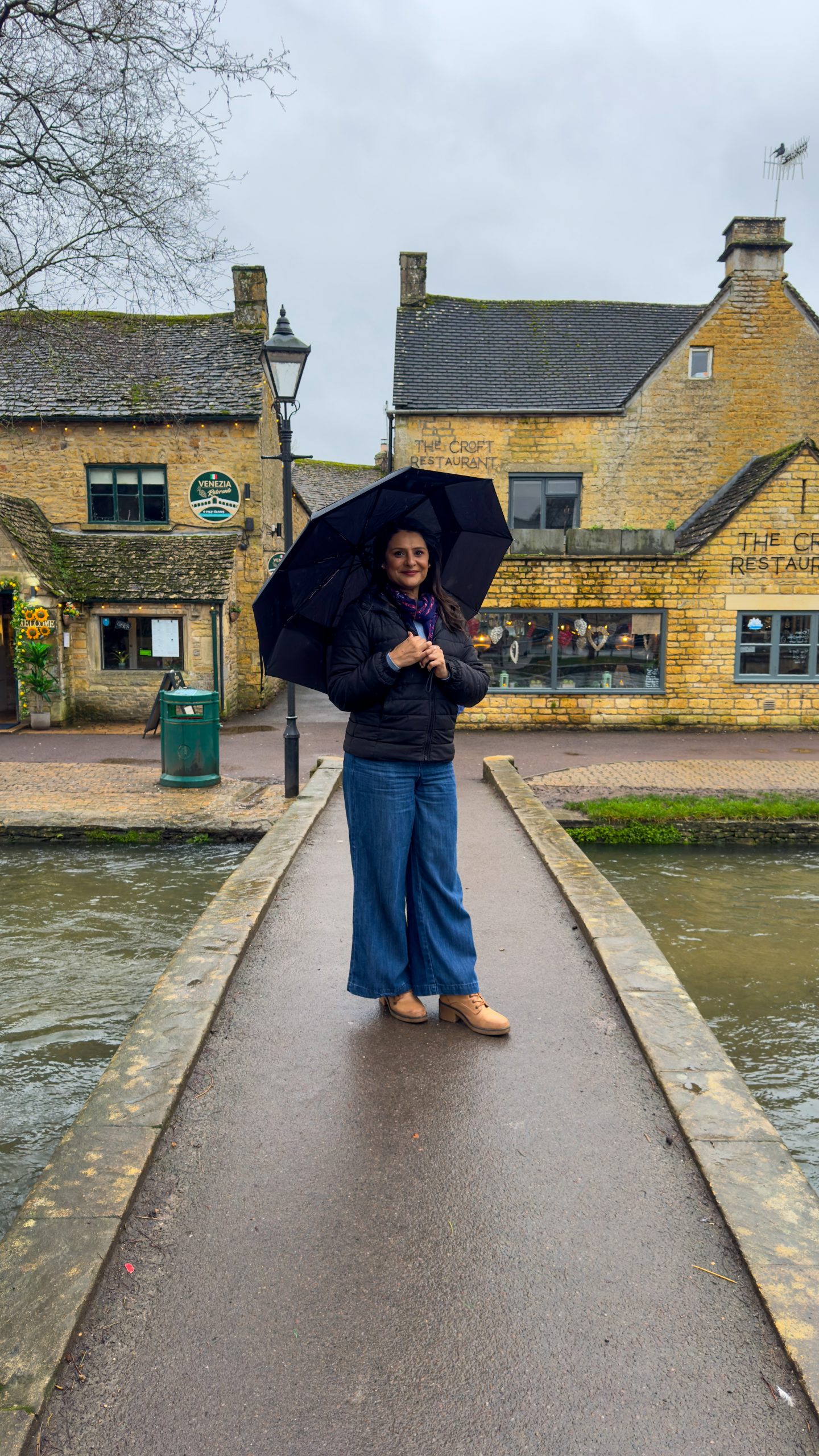 A woman standing in the rain under an umbrella in bourton on the water