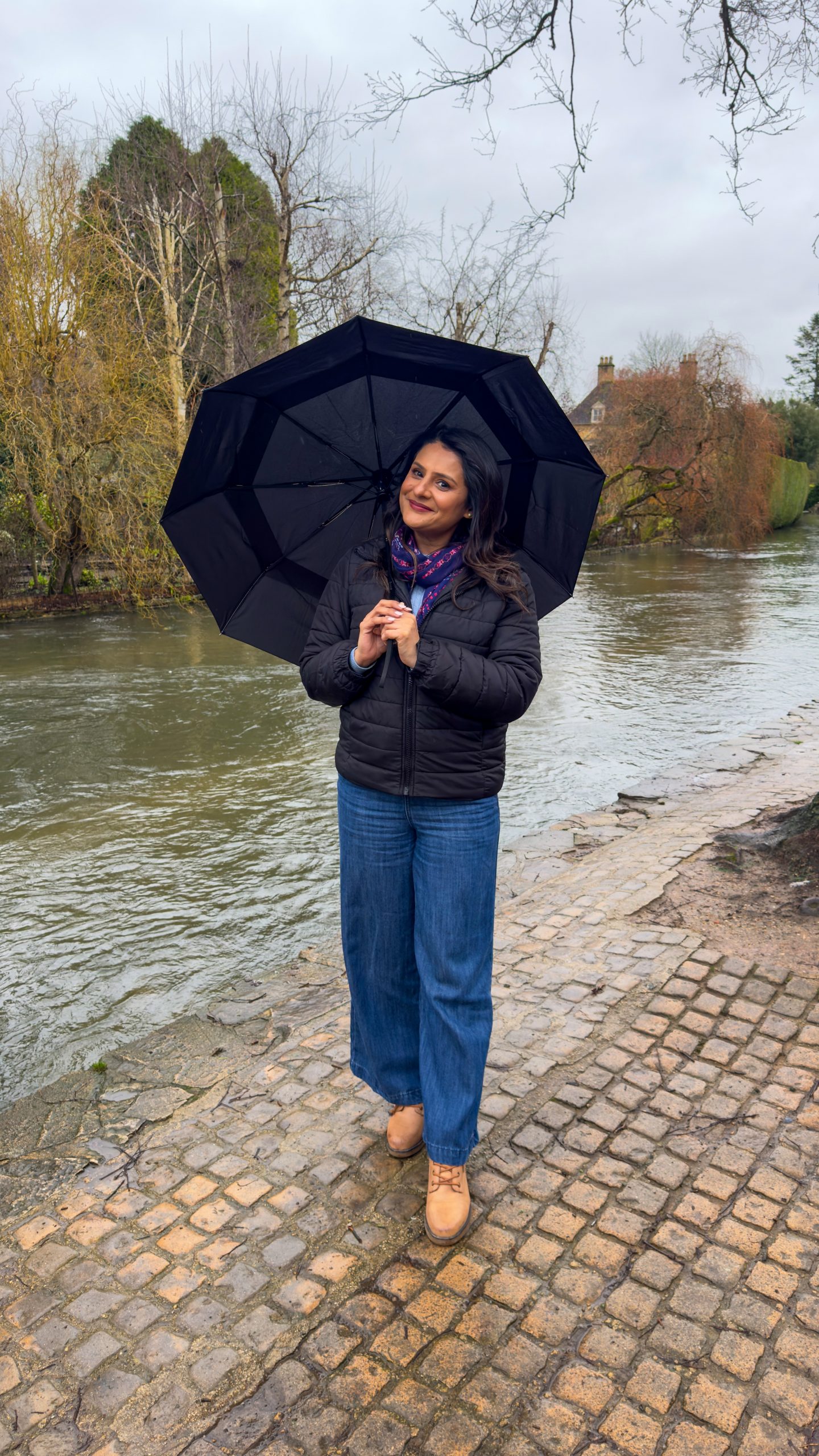 A woman standing in the rain under an umbrella in bourton on the water