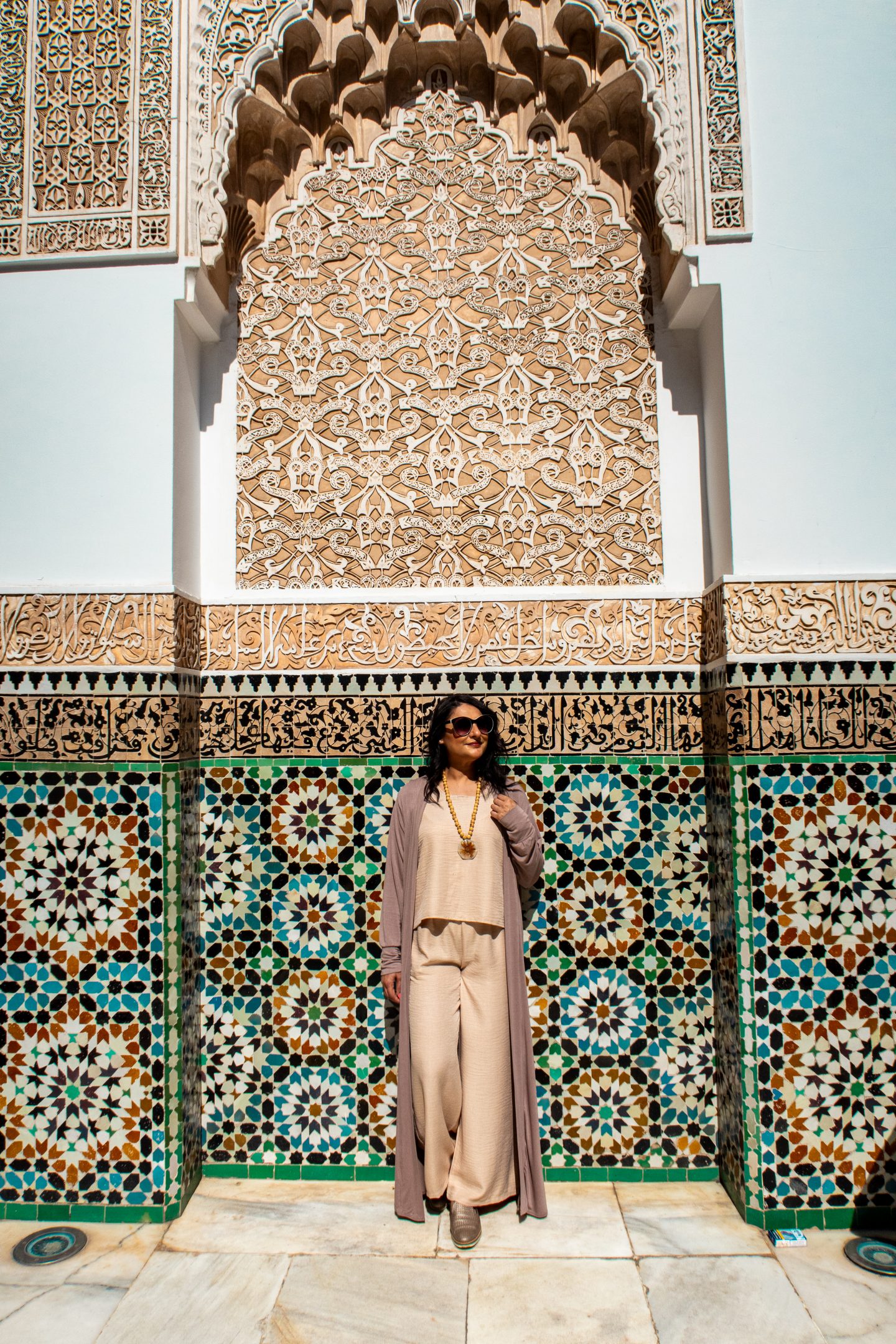 Woman standing in front of intricate tiled wall at Ben Youssef Madrassa