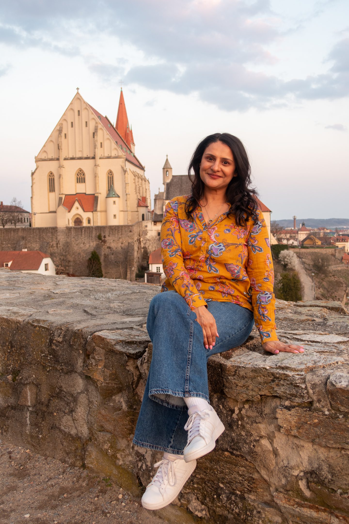 A woman sitting on a wall at sunset with the church in Znojmo in the background
